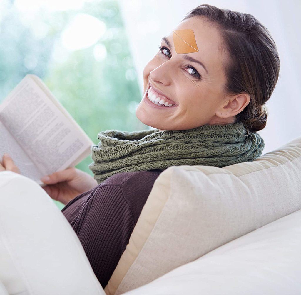 A woman smiling and reading a book while looking at the camera and sitting on a couch.